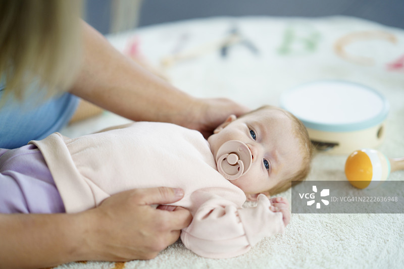 可爱的宝宝在柔软的毯子上安静地休息，嘴里含着安抚奶嘴，身边有玩具。图片素材