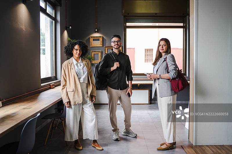 三位年轻专业人士在现代办公室微笑，准备开始他们的工作日图片素材