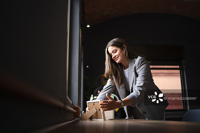 年轻女商人在现代办公室的桌子上摆放相框，为她的工作空间增添个人风格图片素材