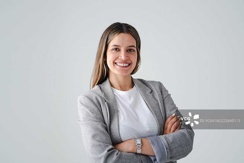 自信的女商人微笑着，双臂交叉，面向镜头，背景为白色。图片素材