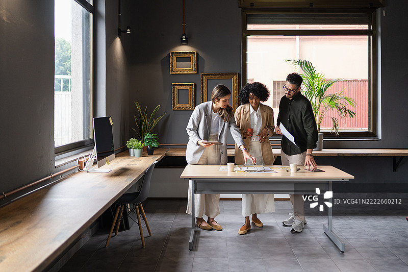 三位设计师在现代办公室环境中合作新项目，审查蓝图并讨论创意。图片素材