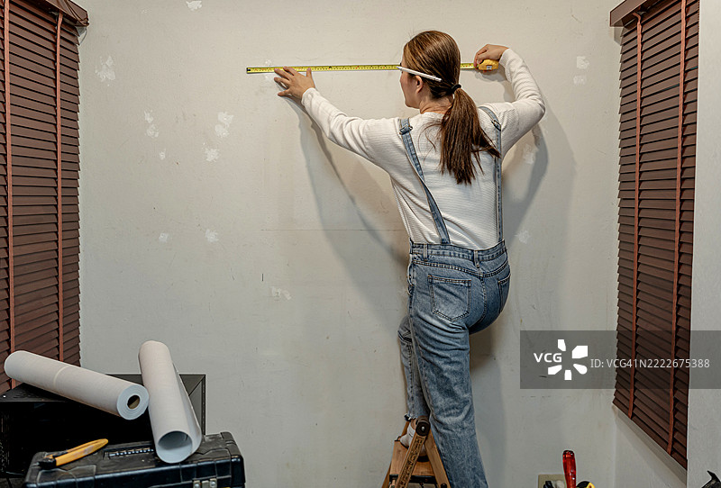 亚洲女性在客厅贴壁纸。DIY和家居装饰。图片素材