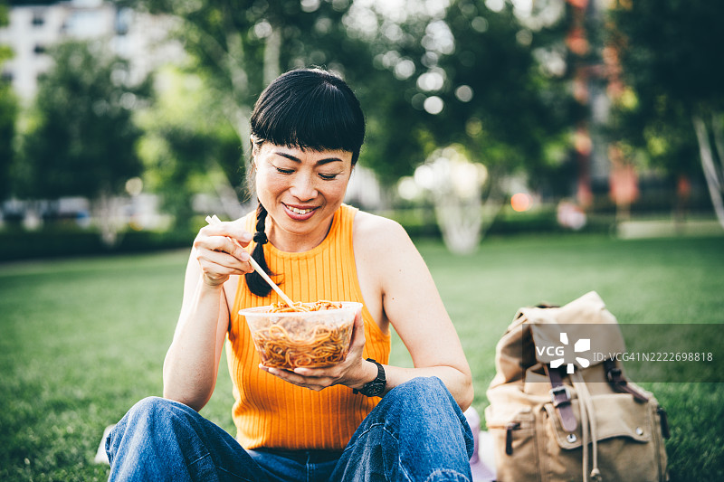 亚洲女性在公园里吃面条。图片素材