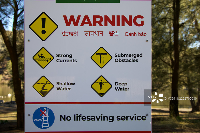 多语言警告标志，位于河边，内容为：“警告：水流湍急，水浅，水下物体，深水。没有救生服务。”图片素材