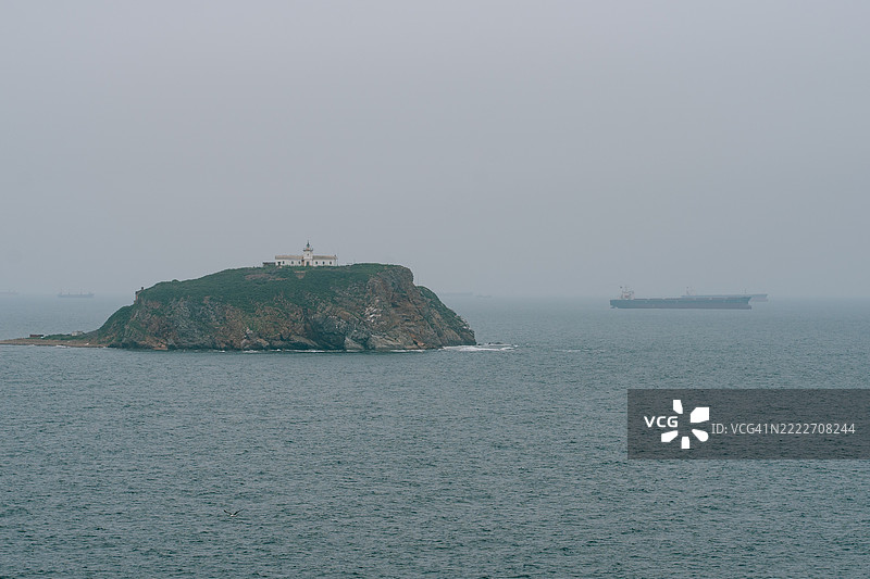 灯塔矗立在岛上，货船在雾蒙蒙的海面上航行图片素材