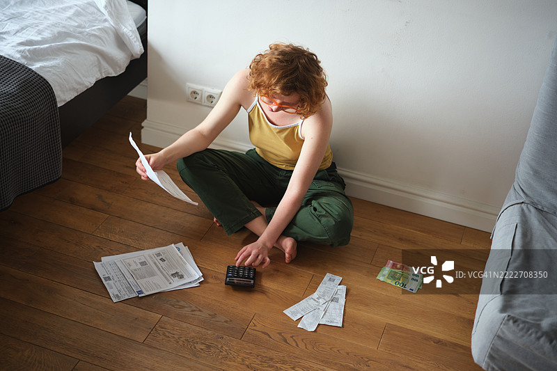 Z世代女孩坐在地板上用计算器计算家庭账单。生活成本图片素材