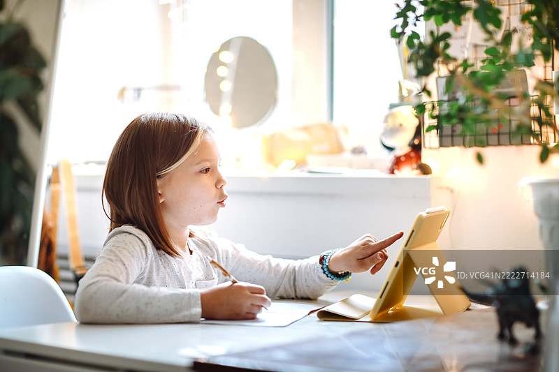 孩子在木桌上独立学习，身边有笔记本、平板电脑和学习用品。图片素材