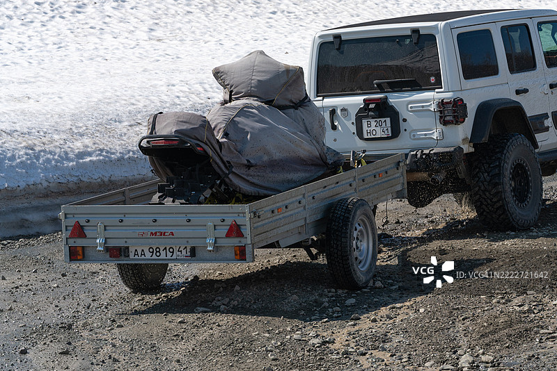 裁剪后的后视图，展示了一辆搭载雪地摩托的吉普牧马人Rubicon在泥土山路上行驶。图片素材