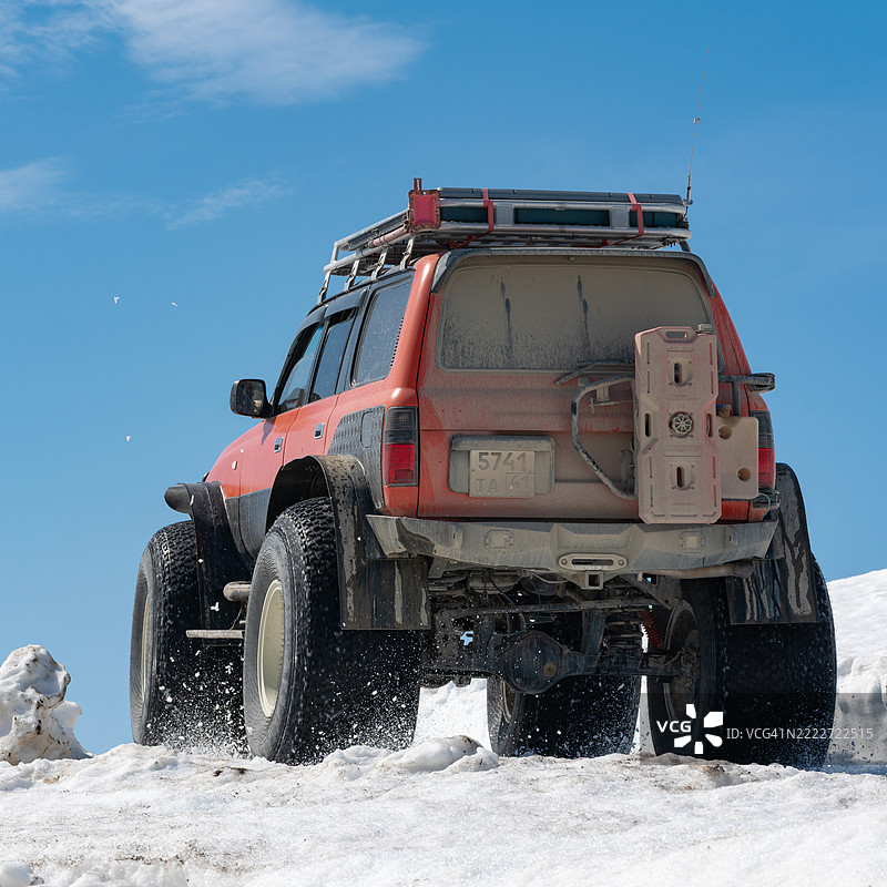 丰田兰德酷路泽SUV在阳光明媚的日子里，驾驶在雪山上的雪地道路上，配备超低气压轮胎。图片素材