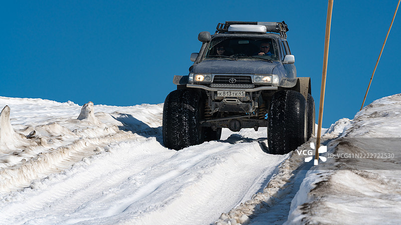 四轮驱动的丰田兰德酷路泽在阳光明媚的日子里，驾驶着超低气压轮胎穿越雪-covered的山区路线。图片素材