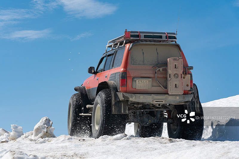 阳光明媚的日子里，丰田陆地巡洋舰在雪覆盖的山路上行驶，后视图显示其超低气压轮胎。图片素材