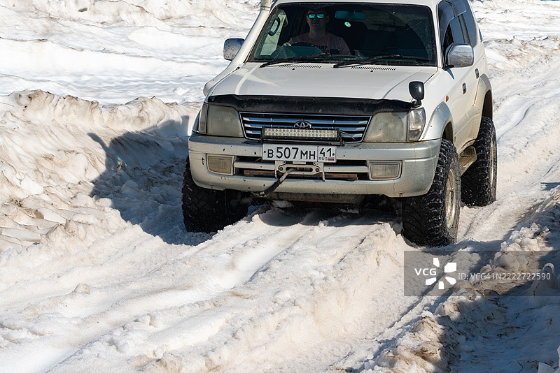 丰田兰德酷路泽普拉多在阳光明媚的日子里行驶在被雪覆盖的山路上。图片素材