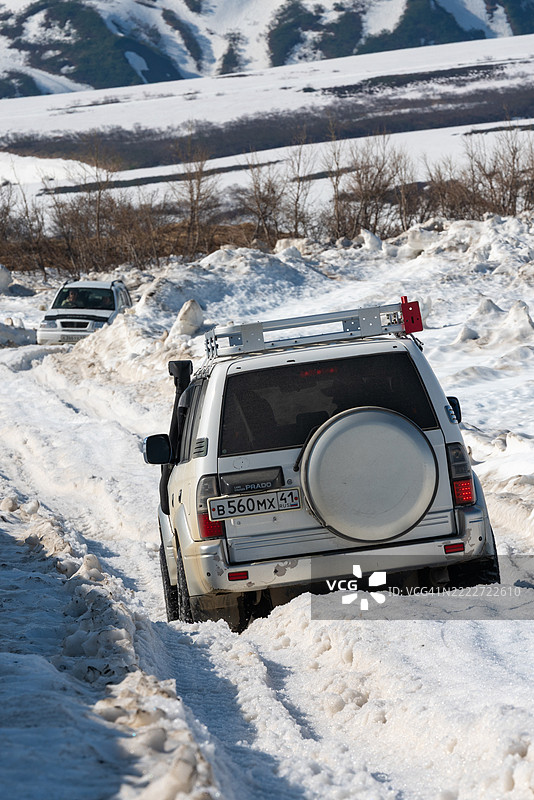 丰田兰德酷路泽普拉多的后视图在阳光明媚的日子里穿越被雪覆盖的山地道路。图片素材