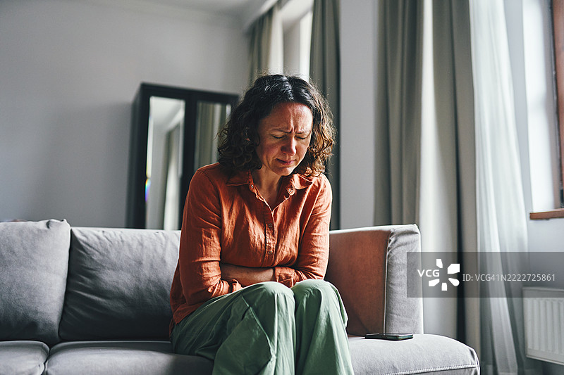 坐在沙发上捂着肚子的沮丧女性室内场景图片素材