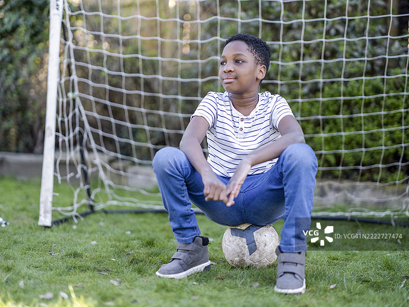 男孩（8-9岁）坐在后院的足球上图片素材