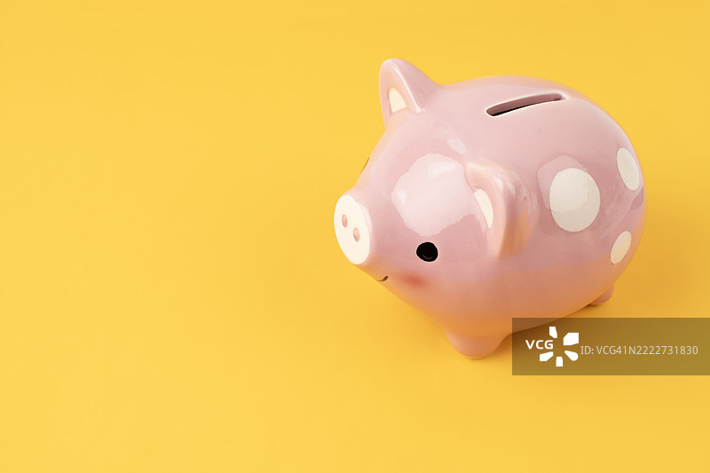 黄色背景上的粉色储蓄罐，留有空白空间。金融、科技、商业分析概念。图片素材
