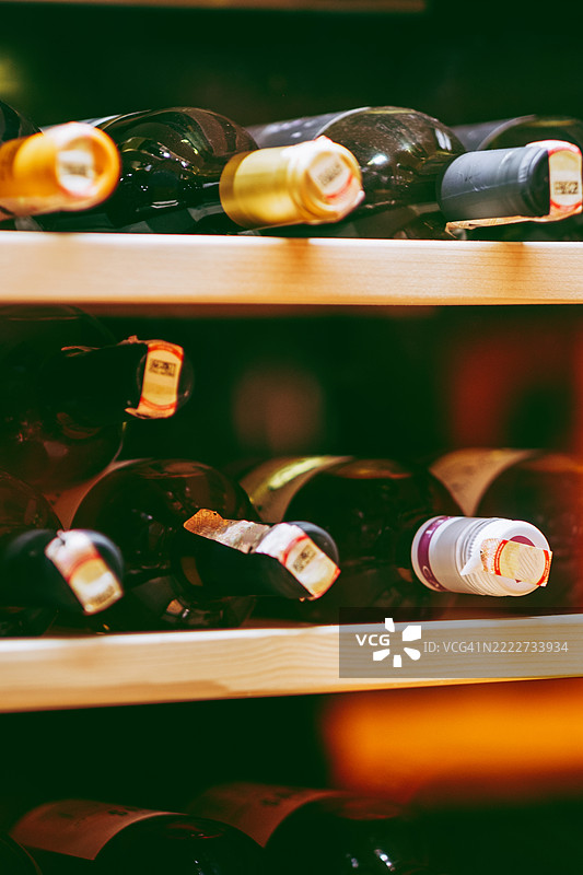 酒瓶存放在昏暗的酒窖木架上。瓶颈特写，标签清晰可见。图片素材