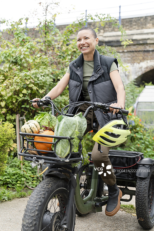 微笑的女性骑着装满自家种植蔬菜的电动货运三轮车图片素材