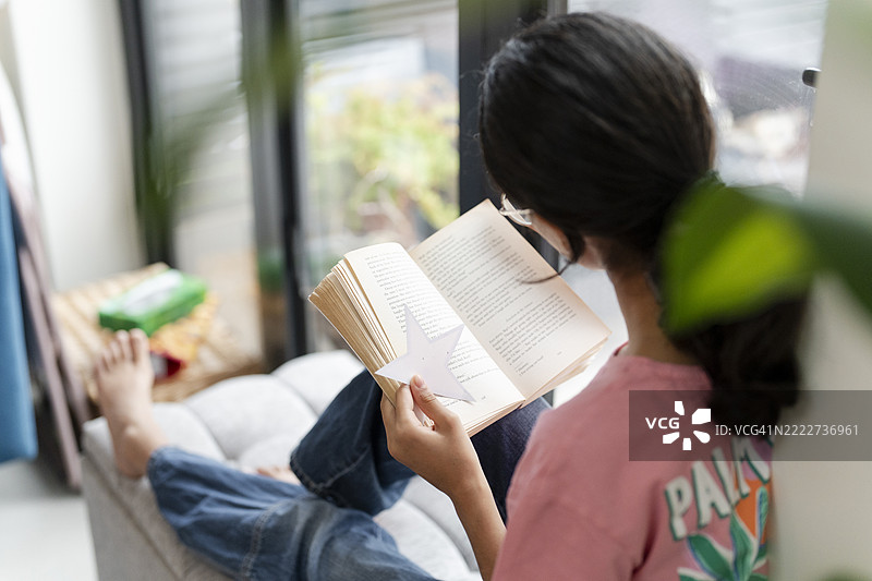 女孩坐在窗边的脚凳上阅读一本书图片素材