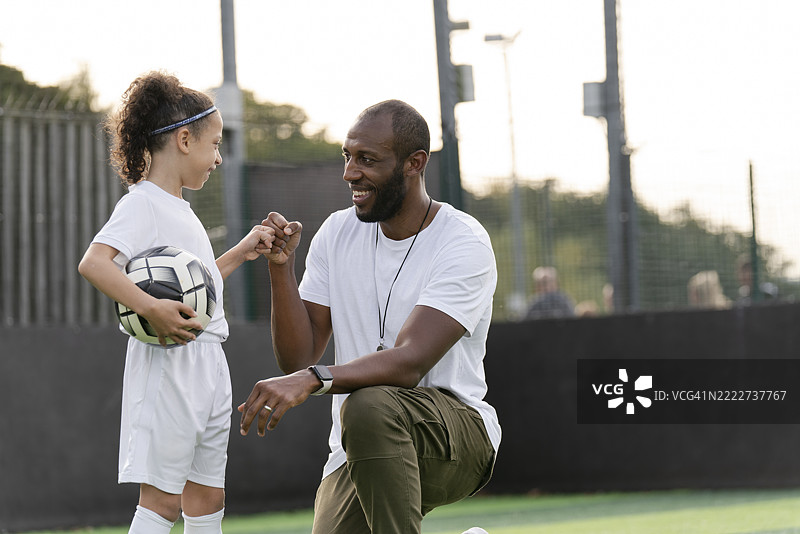 男子在足球场上指导女孩（6-7岁）踢球图片素材