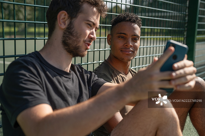 两个男人在网球场上看智能手机图片素材