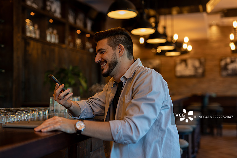 年轻的商务人士在酒吧里使用智能手机并微笑图片素材