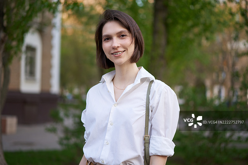户外微笑年轻女性的肖像，背景有树木和建筑物图片素材
