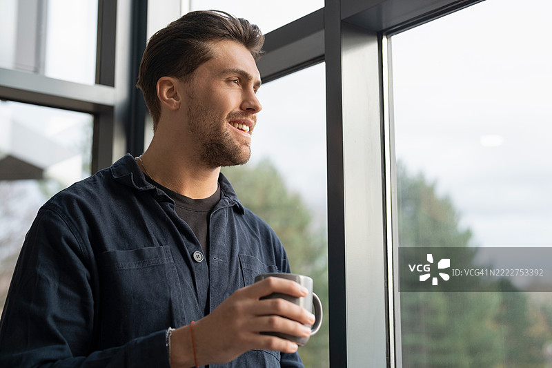 商人喝着咖啡，透过办公室窗户向外看。图片素材