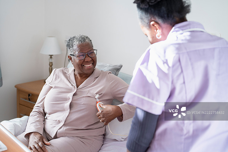 护理人员协助微笑的老年女性坐在床上，手持遥控器图片素材