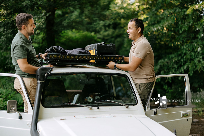 两名冒险者在一辆崎岖的越野车上固定他们的装备图片素材