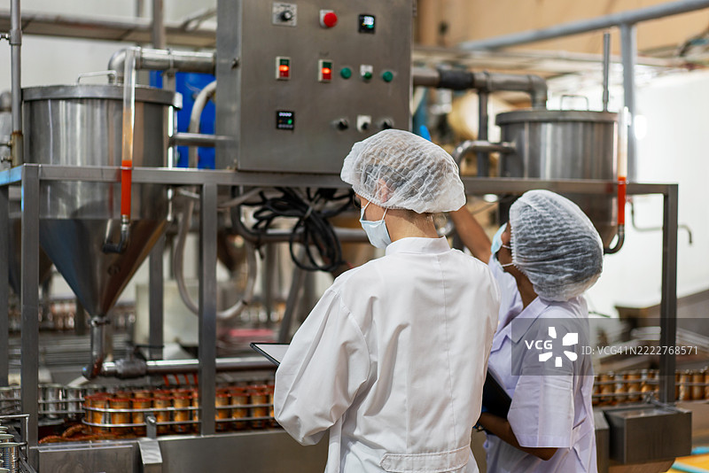 穿着发网和无菌制服的食品科学家和质量控制员正在检查罐装鱼的生产线，以确保产品质量和安全。图片素材