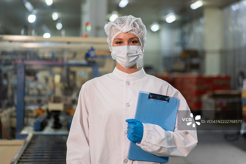 穿着发网和无菌制服的食品科学家和质量控制员正在检查罐装鱼的生产线，以确保产品质量和安全。图片素材