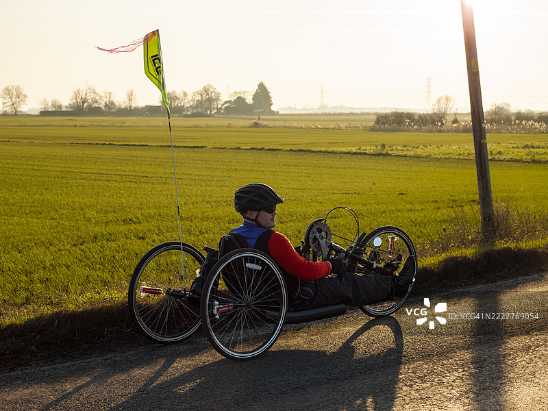 残疾人骑着手动自行车在乡间小路上享受日落图片素材