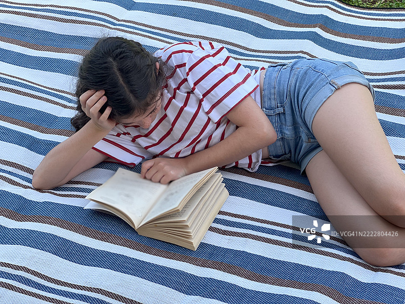 年轻女孩躺在垫子上在家后院阅读一本书图片素材