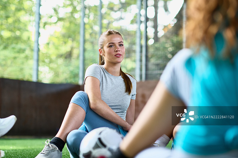 女足球运动员坐在地上拉伸臀部，听着队友的讲话图片素材