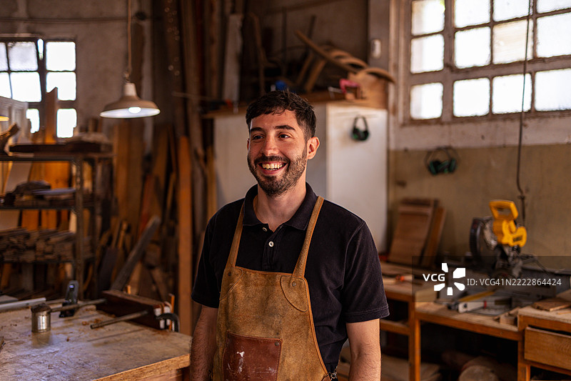 微笑的木匠在乡村风格的工作坊中，周围是工具和木材图片素材