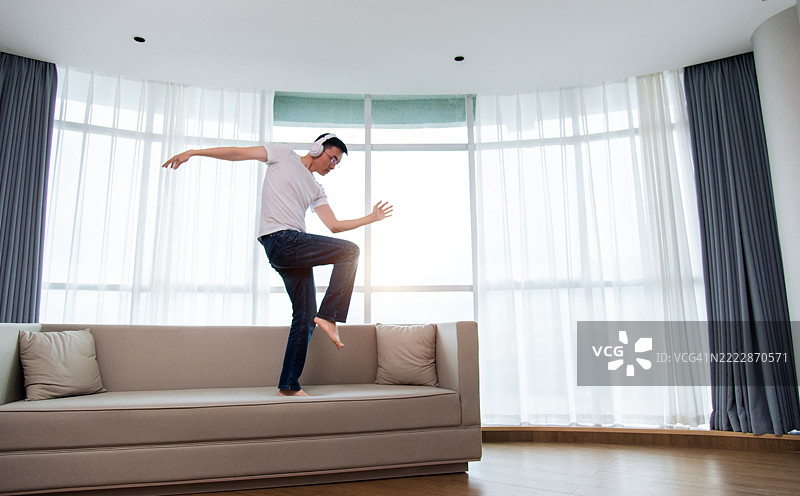 男人戴着耳机在沙发上跳舞图片素材