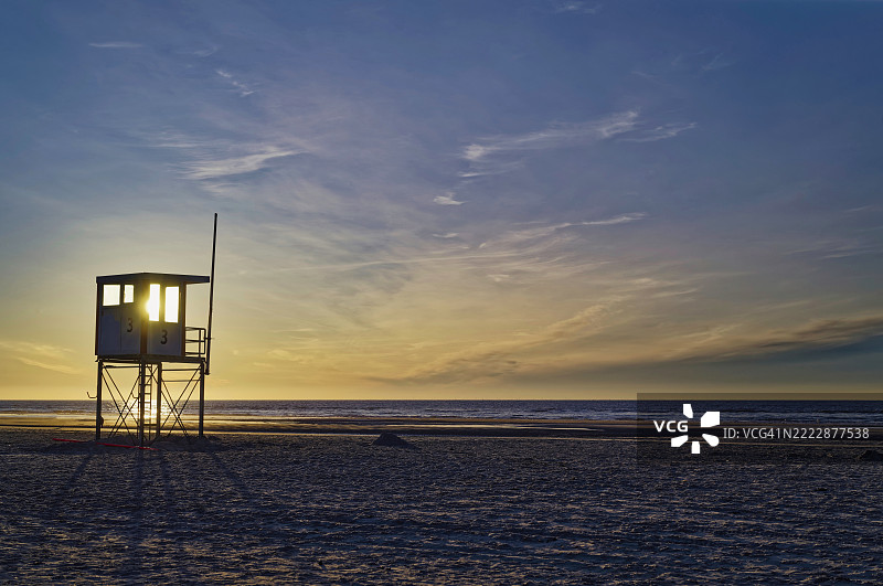 日落时分，德国下萨克森州东弗里西亚地区尤斯特海滩上的救生员小屋剪影图片素材