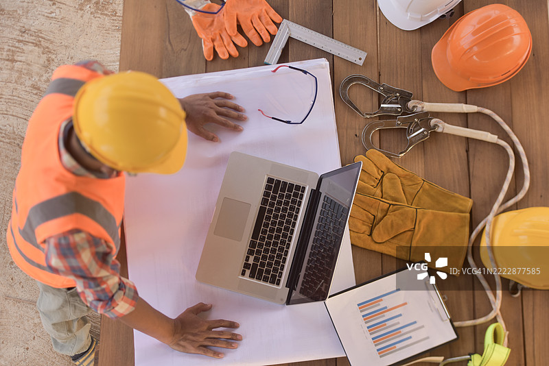 泰国一名建筑工人在桌子旁站着，查看他的笔记本电脑的俯视图图片素材