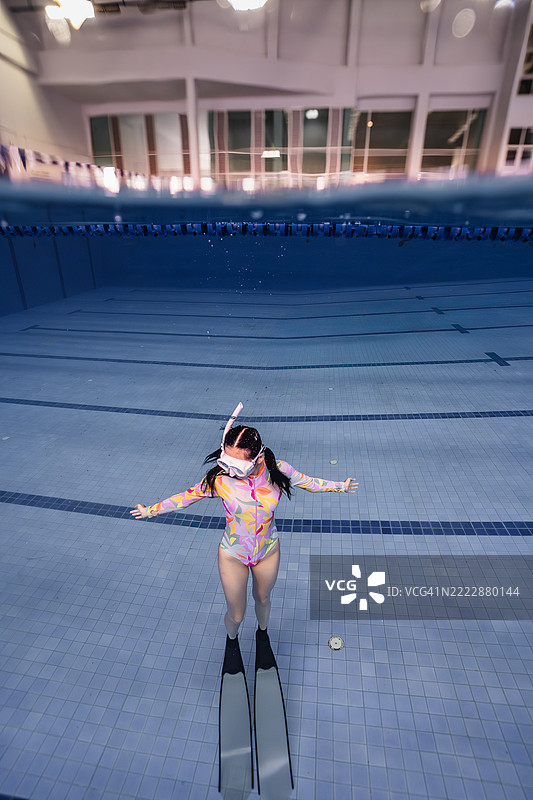 艺术感十足的水下照片，展示了一位穿着色彩斑斓泳衣和脚蹼的女性，优雅地在泳池底部摆姿势。图片素材