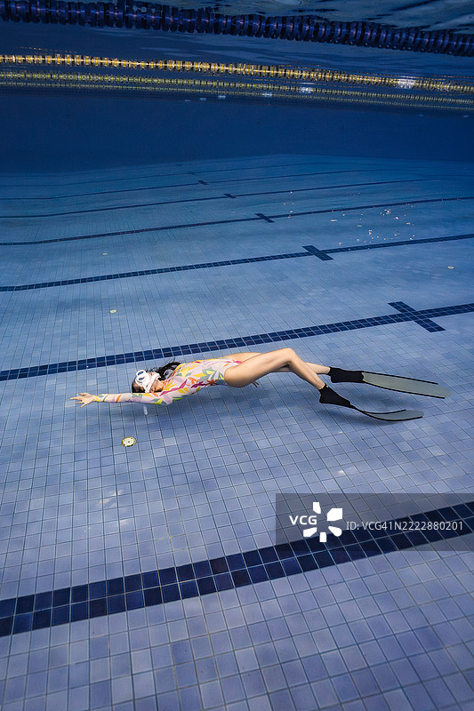 艺术感十足的水下照片，展示了一位穿着色彩斑斓泳衣和脚蹼的女性，优雅地在泳池底部摆姿势。图片素材