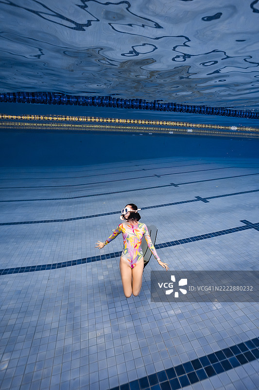 艺术感十足的水下照片，展示了一位穿着色彩斑斓泳衣和脚蹼的女性，优雅地在泳池底部摆姿势。图片素材