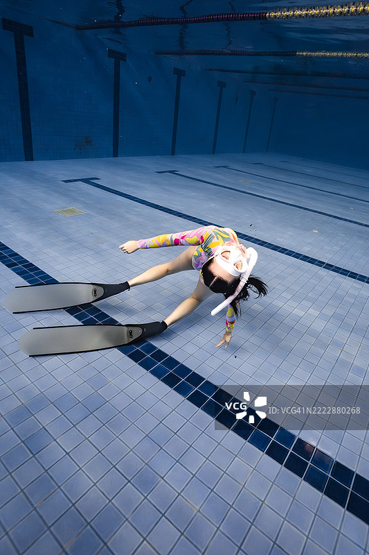 艺术性的水下照片，展示了一位穿着色彩斑斓泳衣和脚蹼的女性，优雅地在泳池底部摆姿势。图片素材