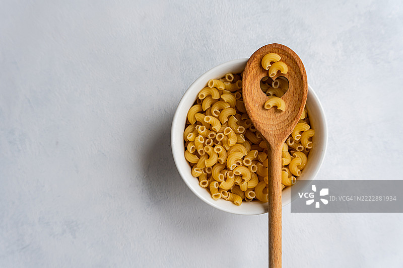 从上方俯视一碗生意大利面和一把木勺，木勺上有一个心形图案，放在厨房工作台上。图片素材