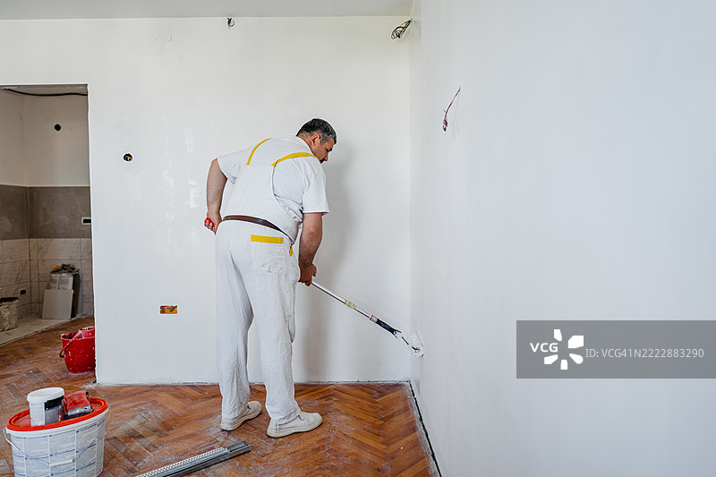成熟的工人在空置的公寓内使用滚筒刷涂墙壁，正在进行装修。图片素材