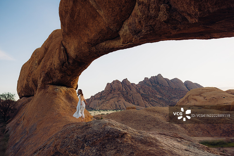 穿着白色裙子的女人在斯皮茨科普自然拱门内晨曦中漫步图片素材