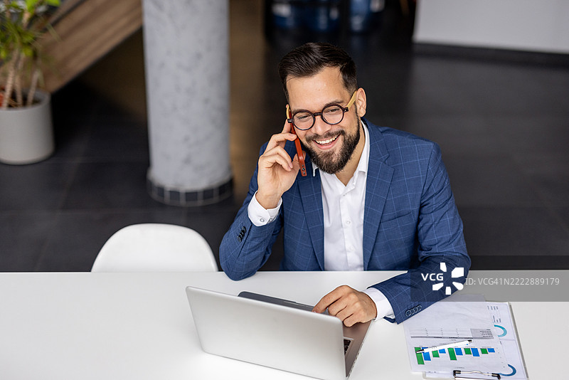 商人在办公室桌子上使用笔记本电脑并打电话图片素材