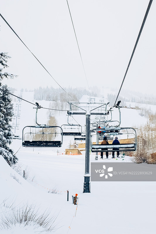两名滑雪者坐在滑雪缆车上，向上升起的雪山。新鲜的雪覆盖了树木和坡道。寒冷的天气，山地交通，滑雪度假村。图片素材