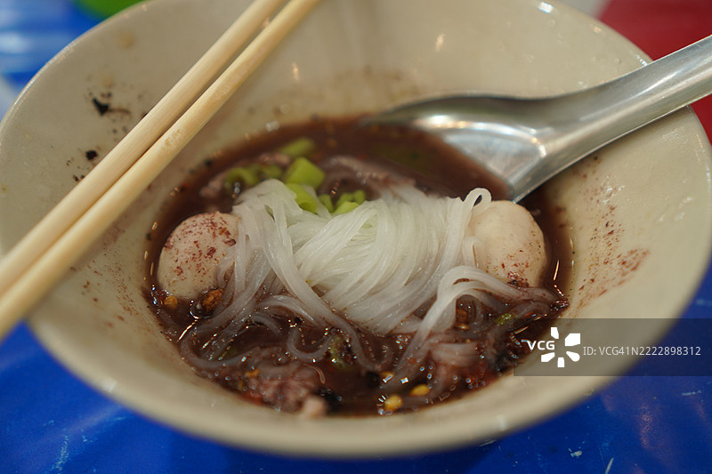 泰式面条，白碗中盛放着小面条、炖猪肉、肉丸、猪肝和血汤，搭配木筷和勺子，调味后美味的泰国菜。图片素材