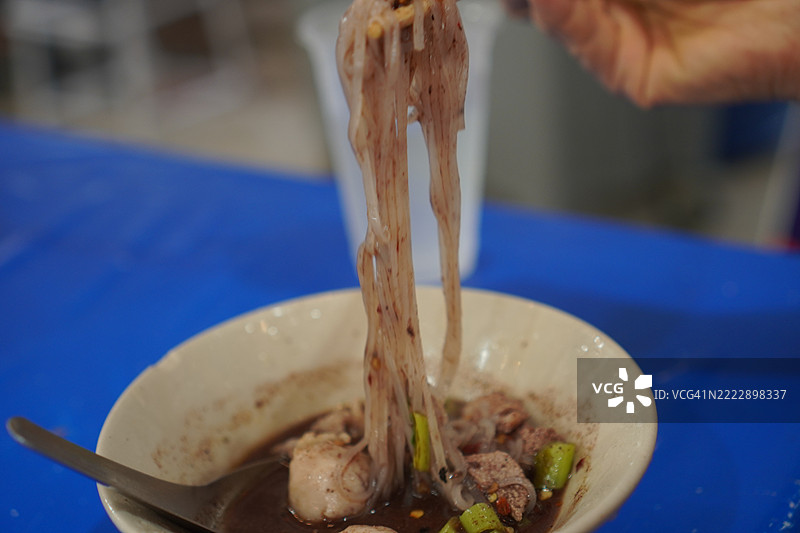泰式面条，白碗中盛着小面条、炖猪肉、肉丸、猪肝和血汤，搭配木筷和勺子，调味后美味的泰国菜。图片素材
